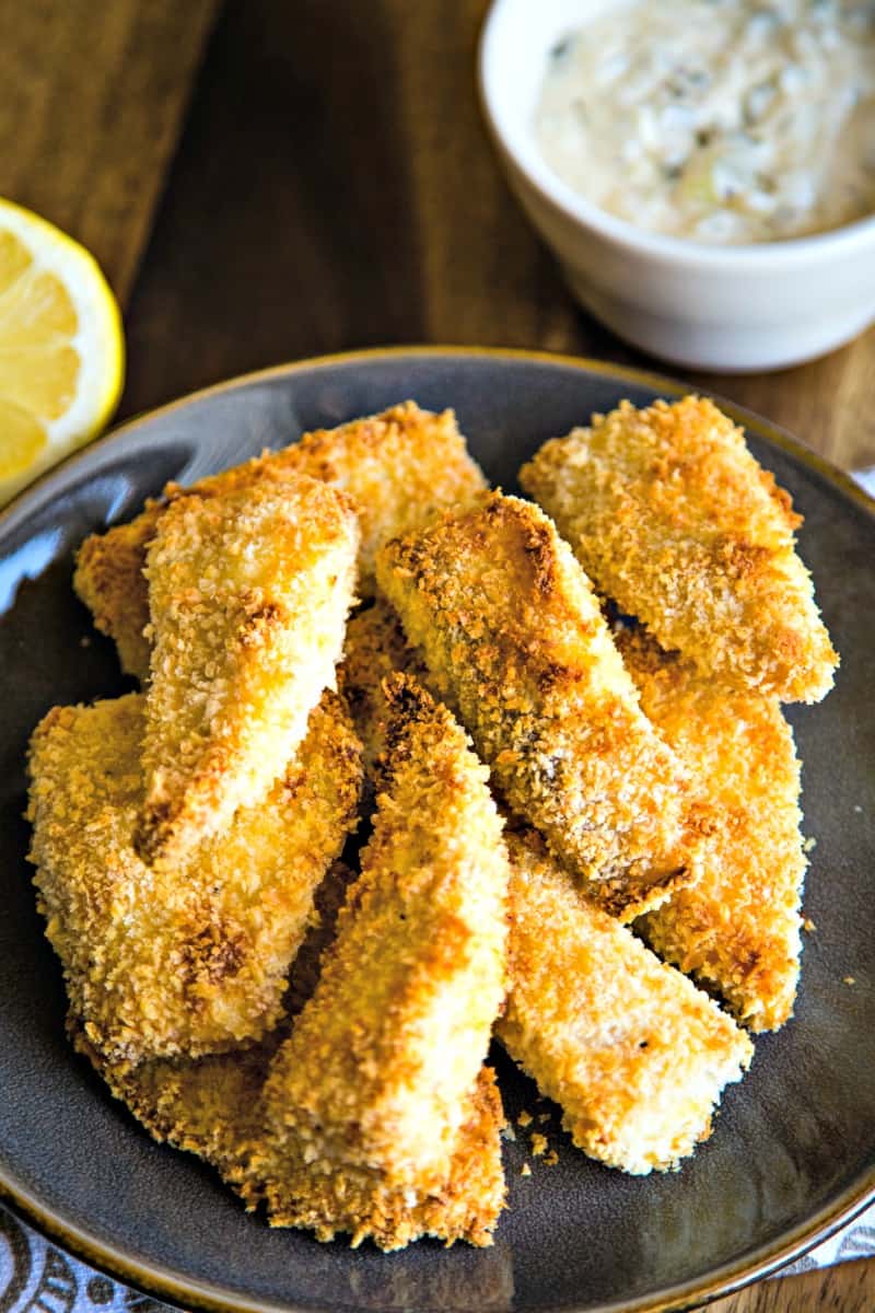 breaded baked fish on a slate plate with lemon and a bowl of tartar sauce