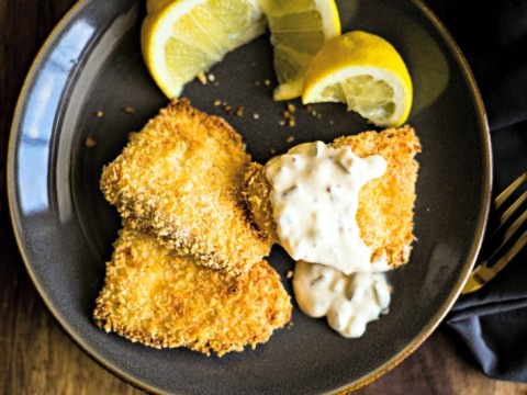 three fish filets with tartar sauce and lemon wedges on a slate plate