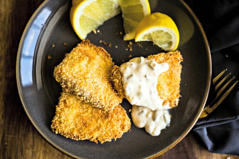 three fish filets with tartar sauce and lemon wedges on a slate plate