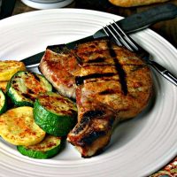 A plate of food on a table, with pork chop and zucchini