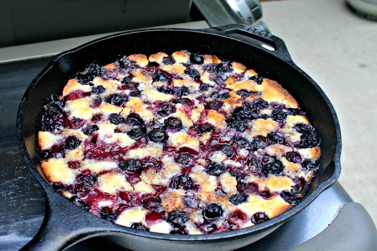 A cast iron skillet sitting on top of a gas grill, with Cherry Berry Cobbler 