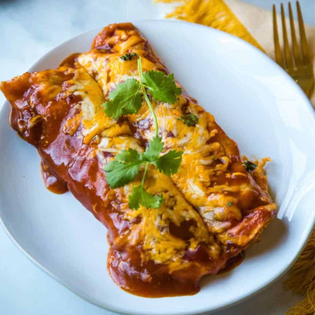 chicken enchiladas with red sauce and cheese on a white plate