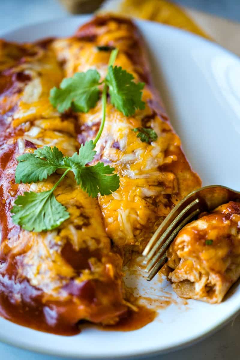 a fork cutting into chicken enchiladas on a plate 