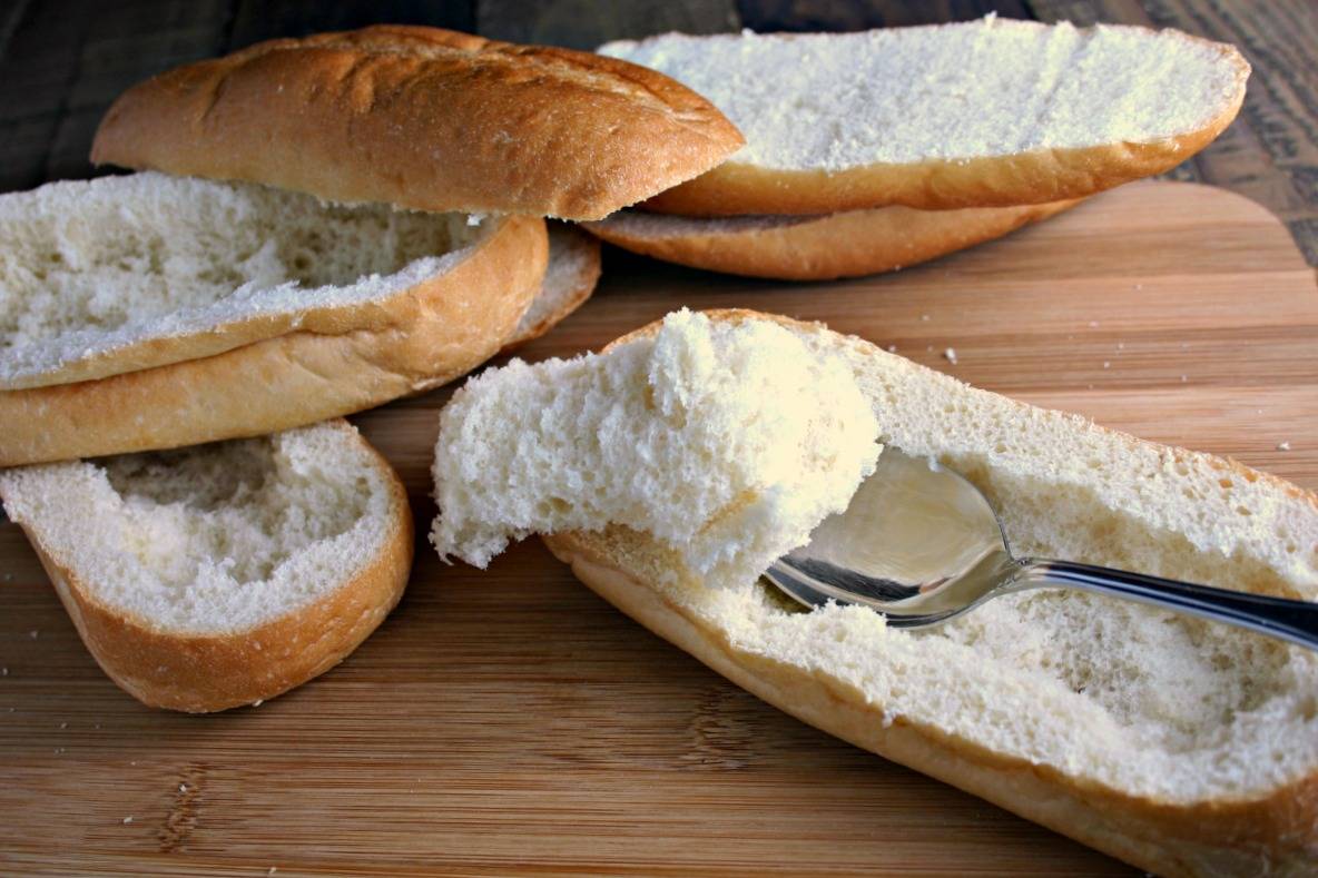 A cut in half sandwich bun sitting on top of a wooden cutting board, with Italian Meatball Subs