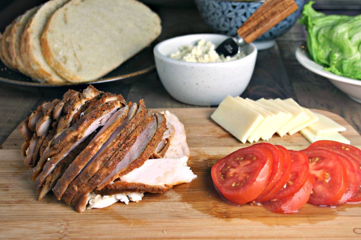 Sliced turkey, tomatoes, and cheese on a wooden cutting board, with Turkey Stack with Feta Spread