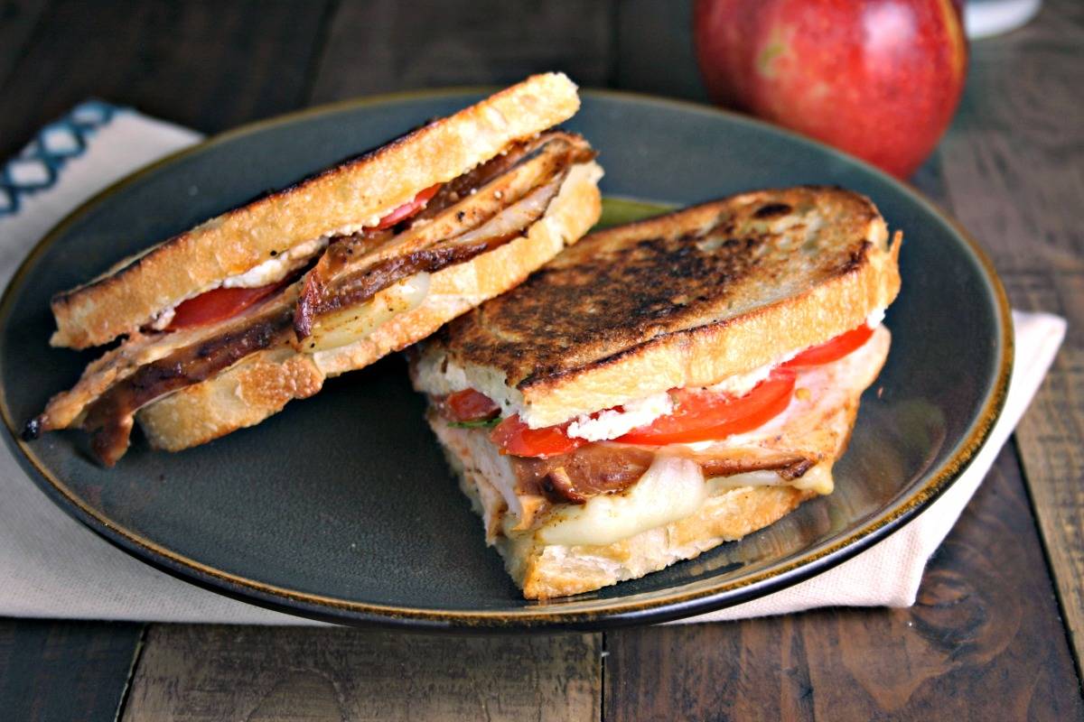 A sandwich cut in half on a plate, with Turkey Stack and Feta Spread