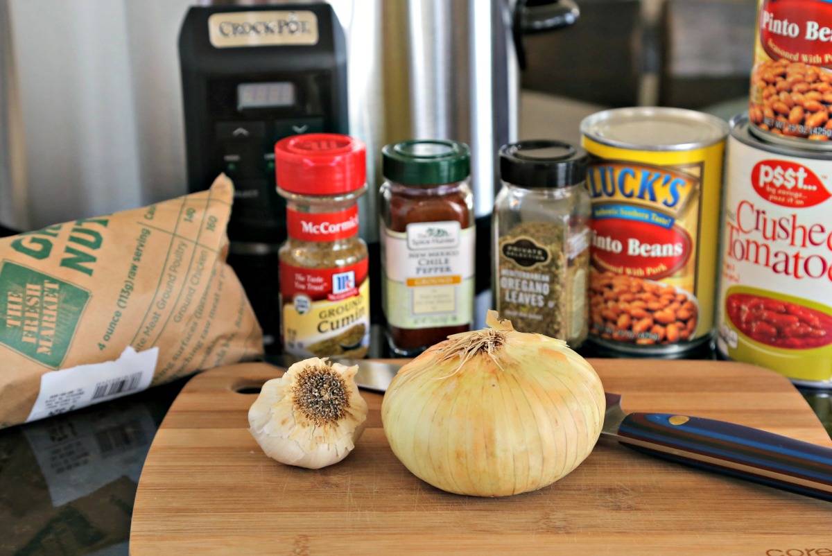 Ingredients for chili on a wooden table, with spices, garlic, onion, and beans