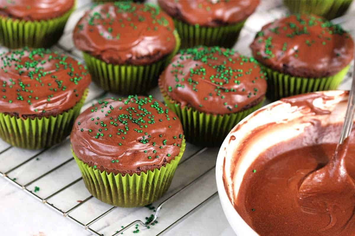 mint cream filled chocolate cupcakes on a wire rack with a bowl of frosting