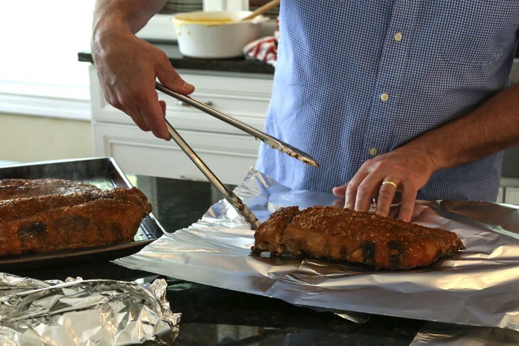 A man wrapping ribs in aluminum foil