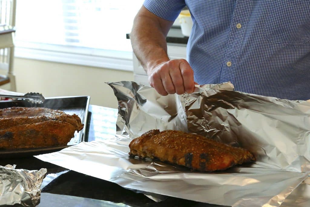 A man wrapping smoked baby back ribs in aluminum foil