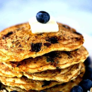 A close up of a stack of blueberry coconut oatmeal pancakes on a plate