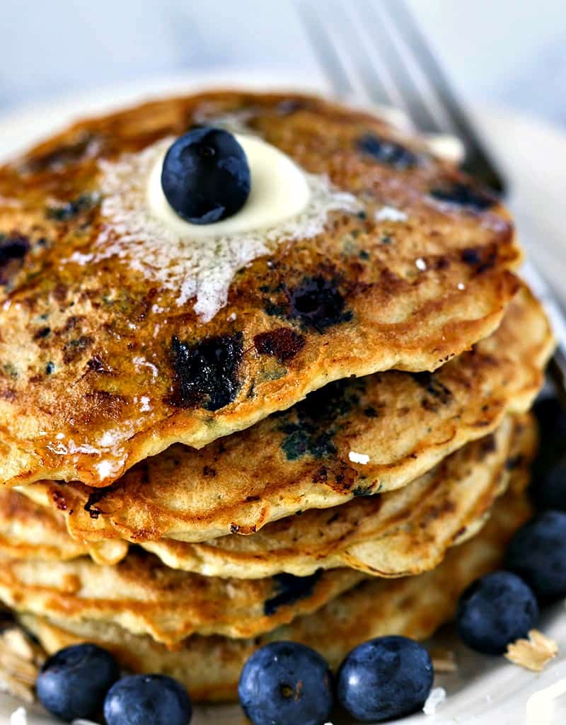 A close up of a stack of blueberry coconut oatmeal pancakes on a plate