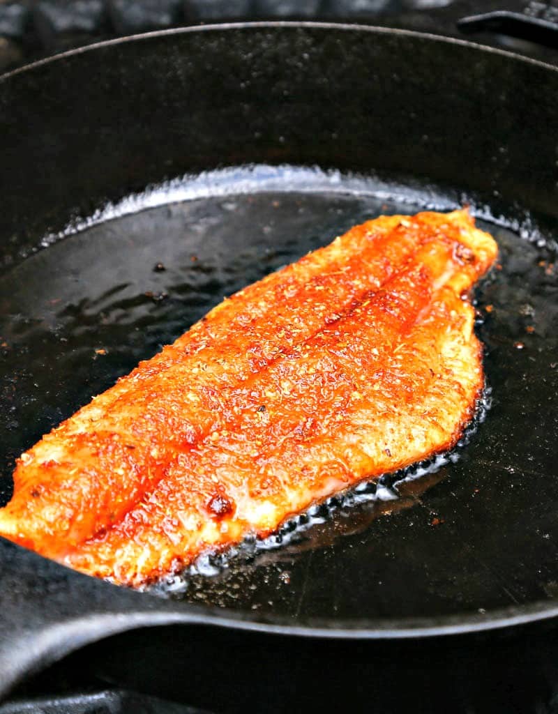 A close up of a cast iron skillet with catfish being cooked