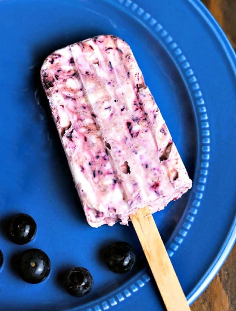 A blueberry cheesecake popsicle on a blue plate