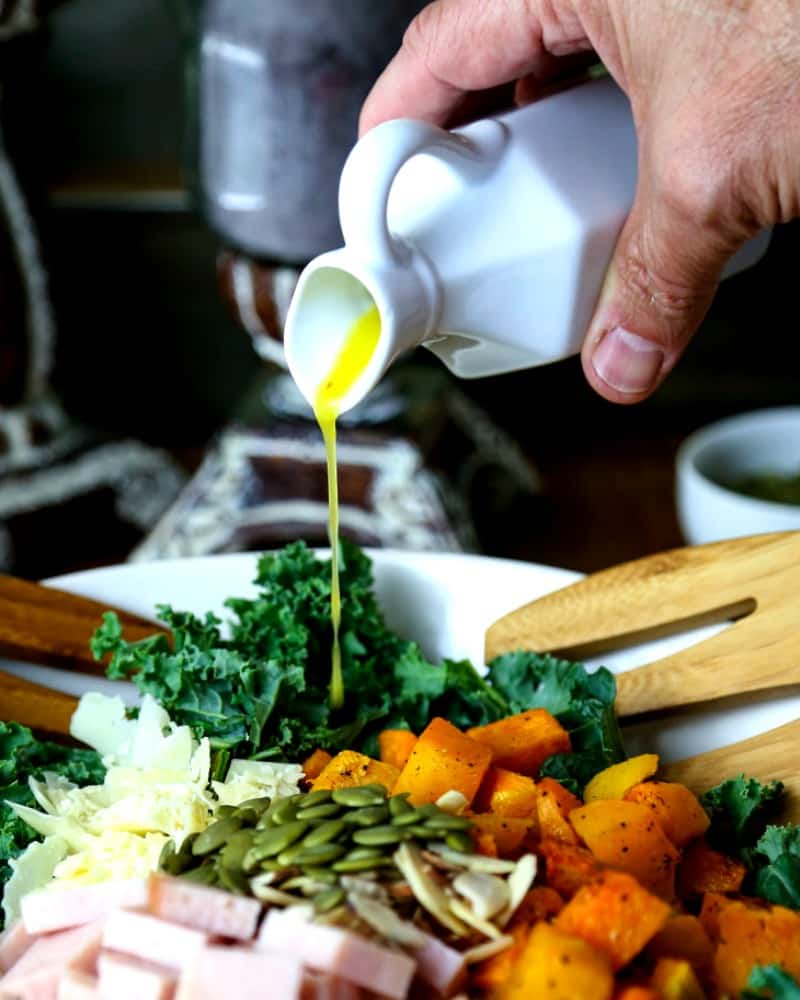 A person pouring dressing on autumn salad with butternut squash, turkey, and kale