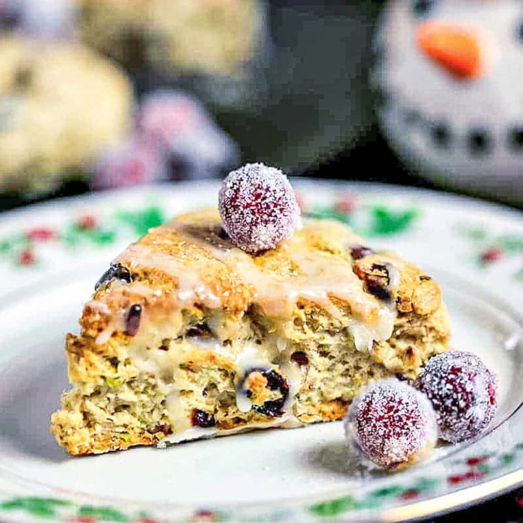 A Cranberry Pistachio Scone garnished with sugared cranberries on a holiday plate.