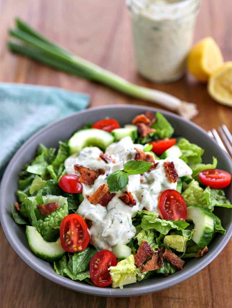 A bowl of salad on a plate, with Basil Buttermilk dressing