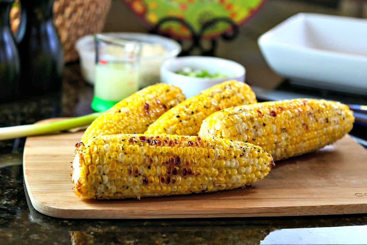 Grilled ears of corn on top of a wooden cutting board