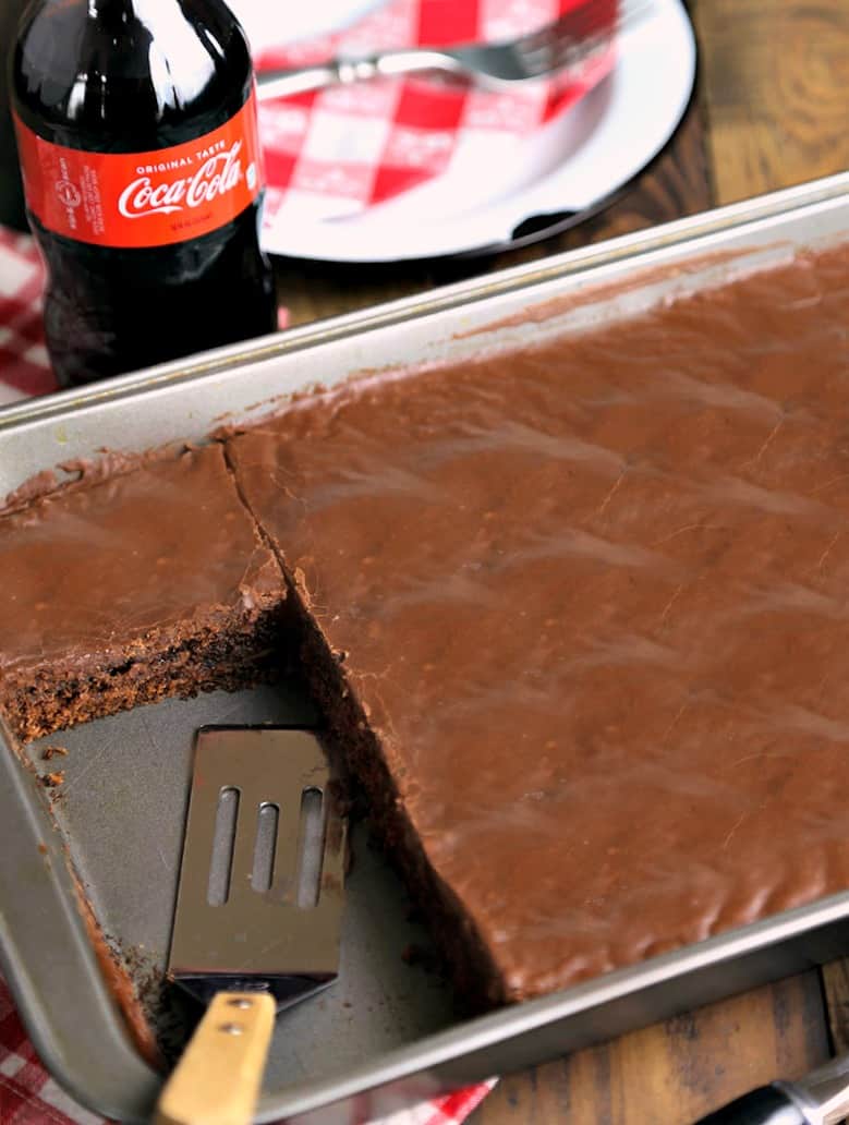 A bottle of Coca Cola on a table with chocolate cake