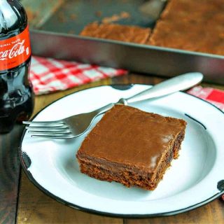 A piece of cake on a plate on a table, with Chocolate Coca-Cola Cake