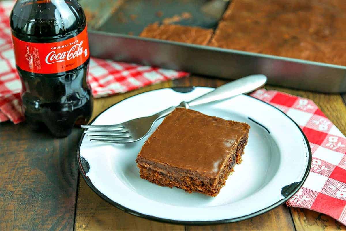 A piece of cake on a plate on a table, with Chocolate Coca-Cola Cake