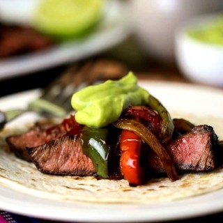 A plate of food on a table, with grilled steak fajitas and guacamole