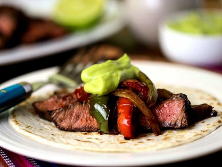 A plate of food on a table, with grilled steak fajitas and guacamole