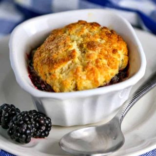 Mini Blackberry Cobbler in a ramekin on a plate with blackberries