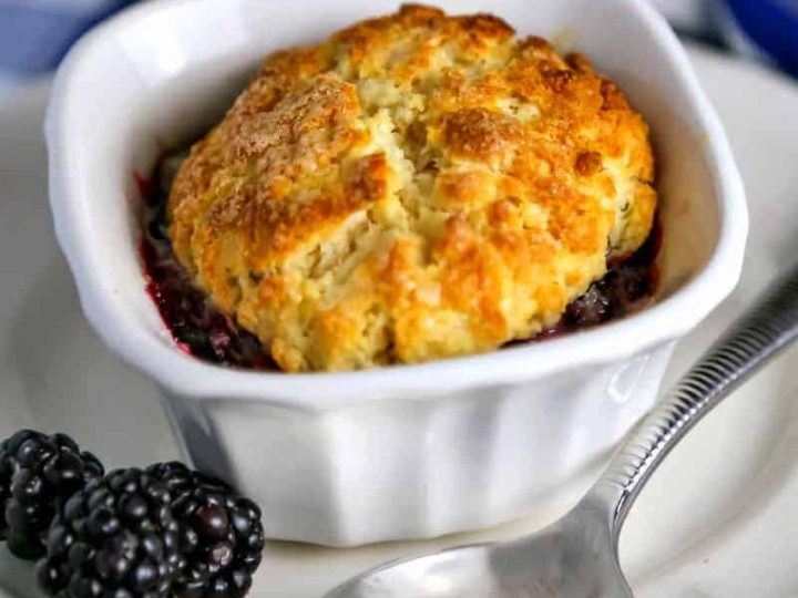 Mini Blackberry Cobbler in a ramekin on a plate with blackberries