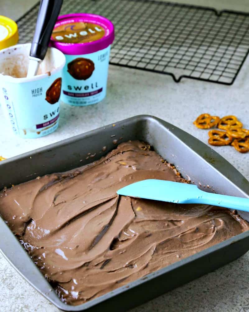 Spreading chocolate ice cream on top of a pretzel crust in a pan