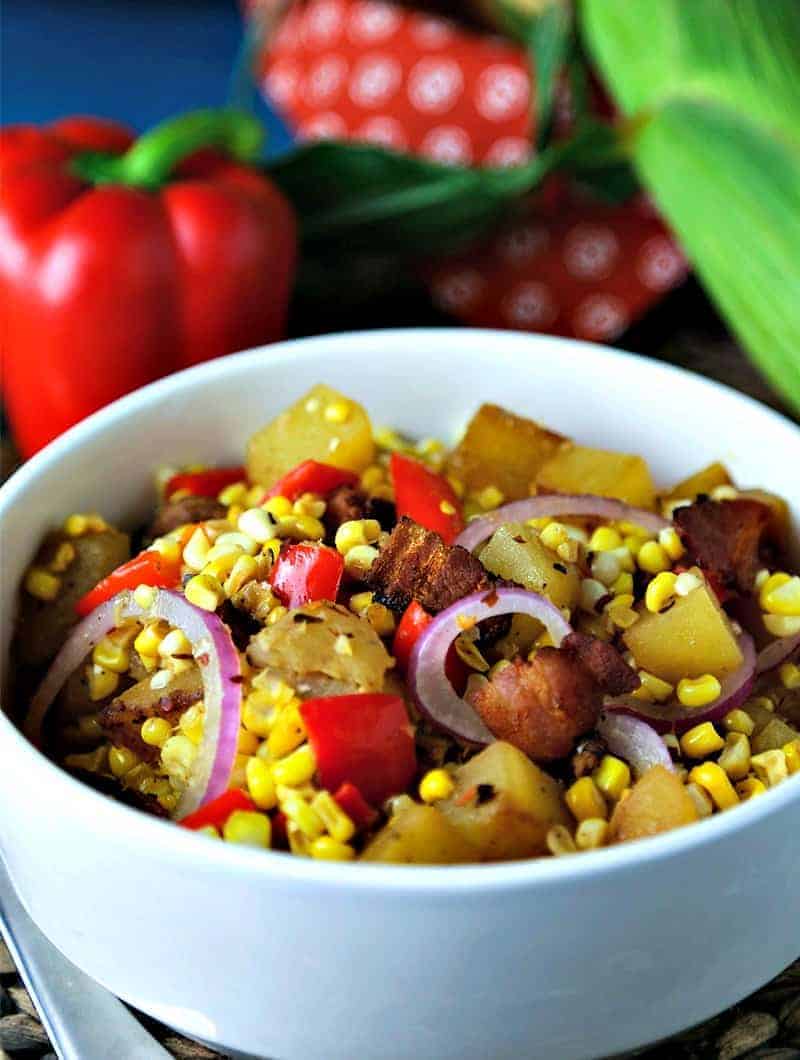 A bowl of food on a plate, with warm corn chowder salad