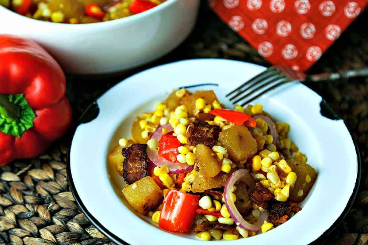 A bowl of food on a plate, with warm corn chowder salad