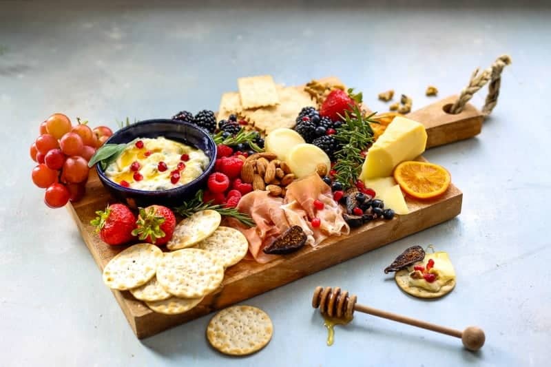 A bunch of food on a cheeseboard, with fruit, berries, and nuts