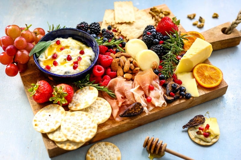 A bunch of food on a cheeseboard, with fruit, berries, and nuts