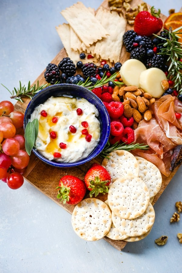 A plate of food on a table, with Cheese, fruit, and crackers