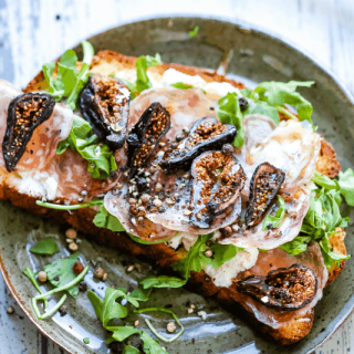A plate of food with a slice of toast, with Ricotta cheese, figs, and arugula