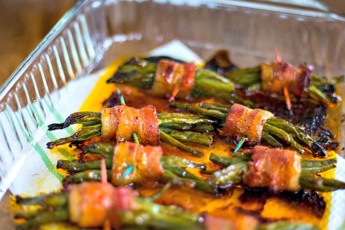 cooked green bean bundles wrapped in bacon in glass dish