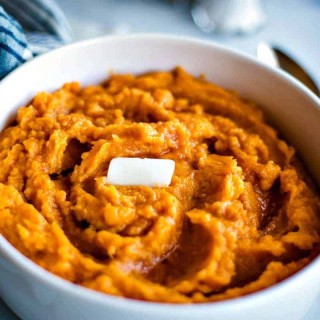 Mashed sweet potatoes with a pat of butter in a white bowl