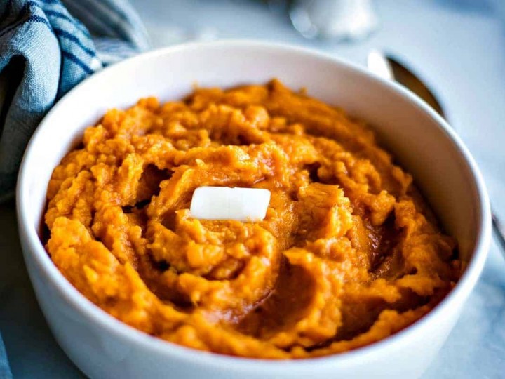 Mashed sweet potatoes with a pat of butter in a white bowl
