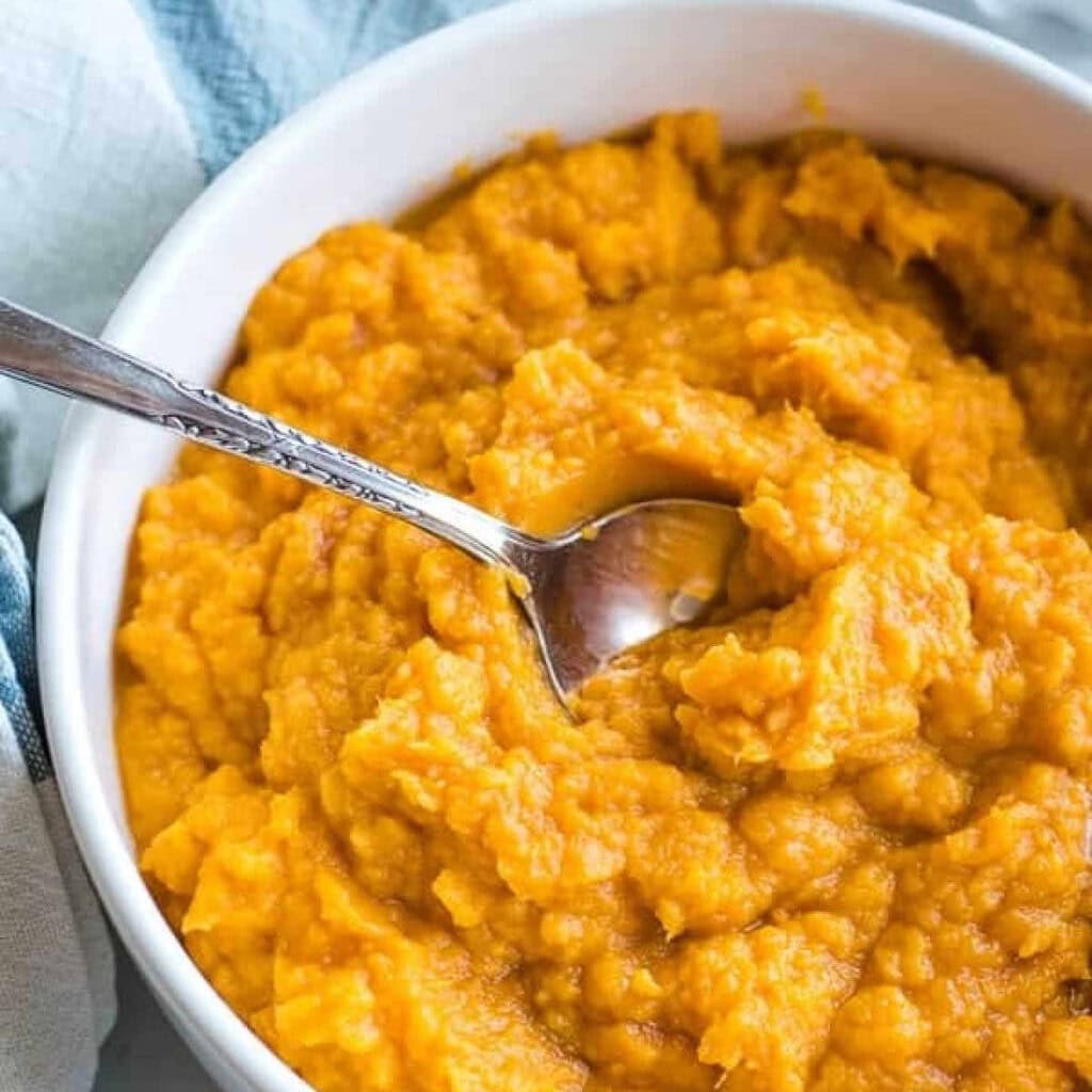 Mashed Sweet Potatoes in a white bowl with a spoon.