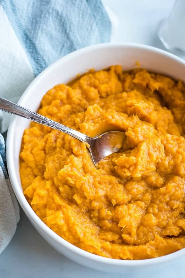 Mashed sweet potatoes in a white bowl with serving spoon