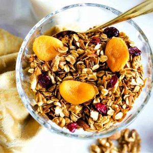 A bowl of homemade granola topped with dried fruit on a table.