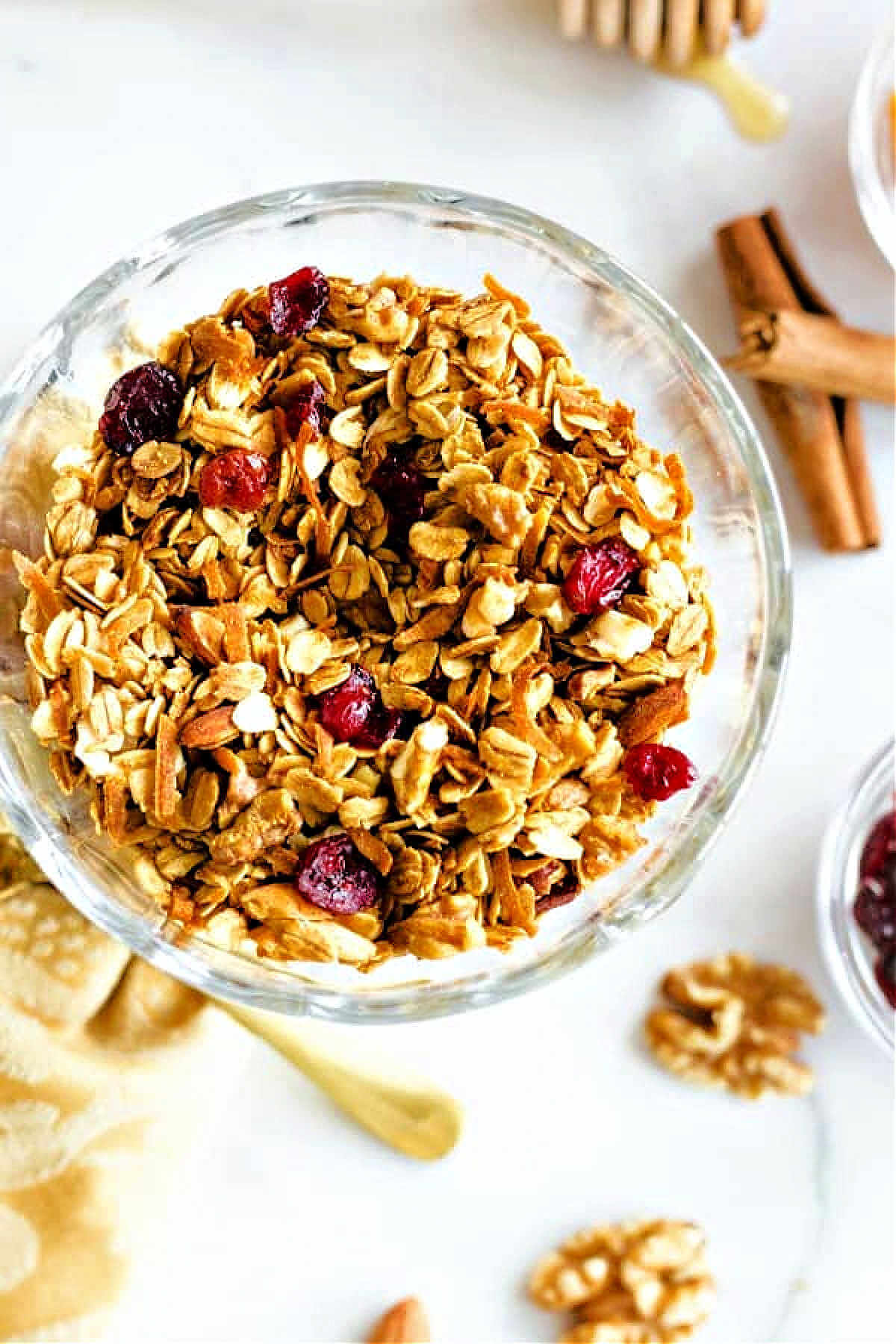 Nut granola in a bowl on a table with cinnamon sticks and walnuts scattered around.