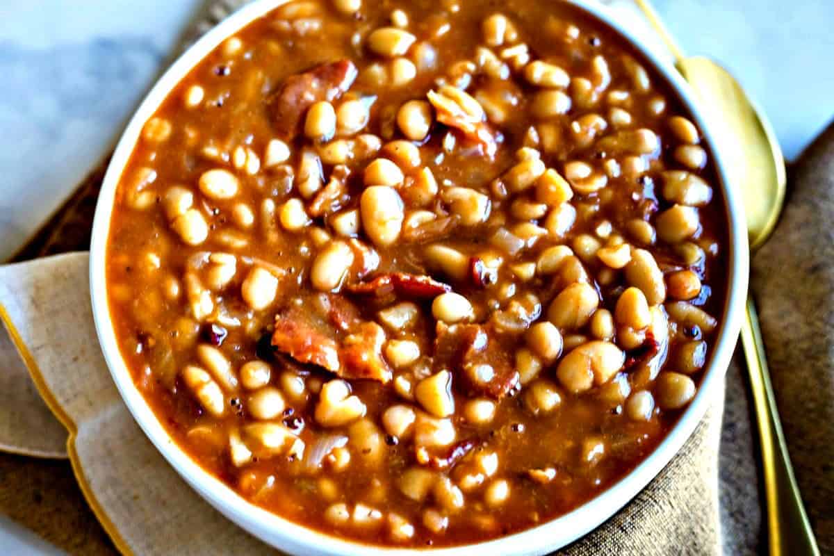 Smoky Chipotle Baked Beans in a white bowl with gold spoon