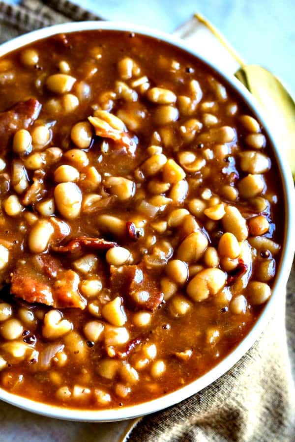 Smoky Chipotle Baked Beans in a white bowl with gold spoon and napkin