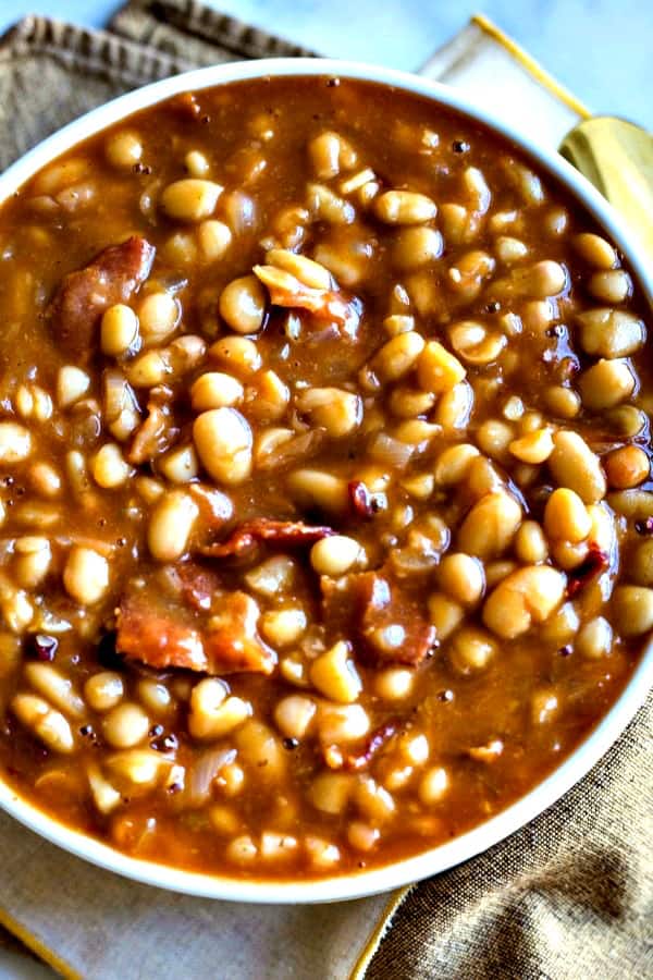 Smoky Chipotle Baked Beans in a white bowl with gold spoon and napkin