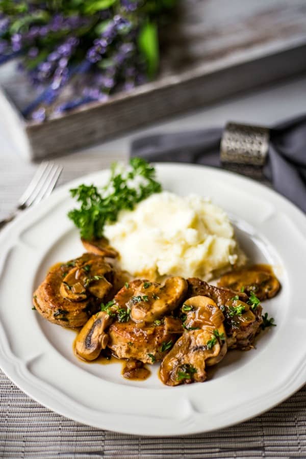 a white dinner plate with pork medallions in mushroom marsala sauce and mashed potatoes