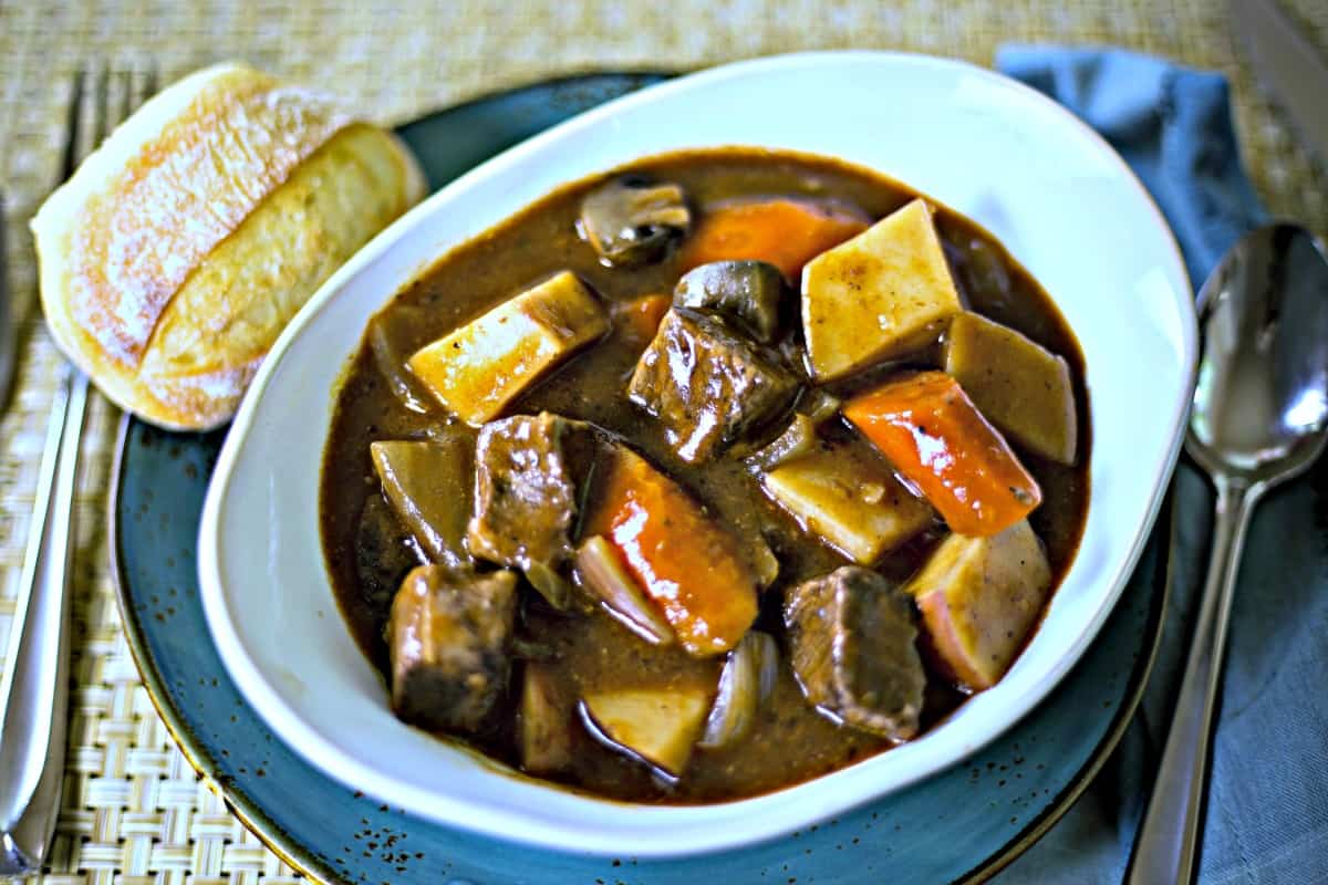 beef stew in a white bowl with a roll on a plate