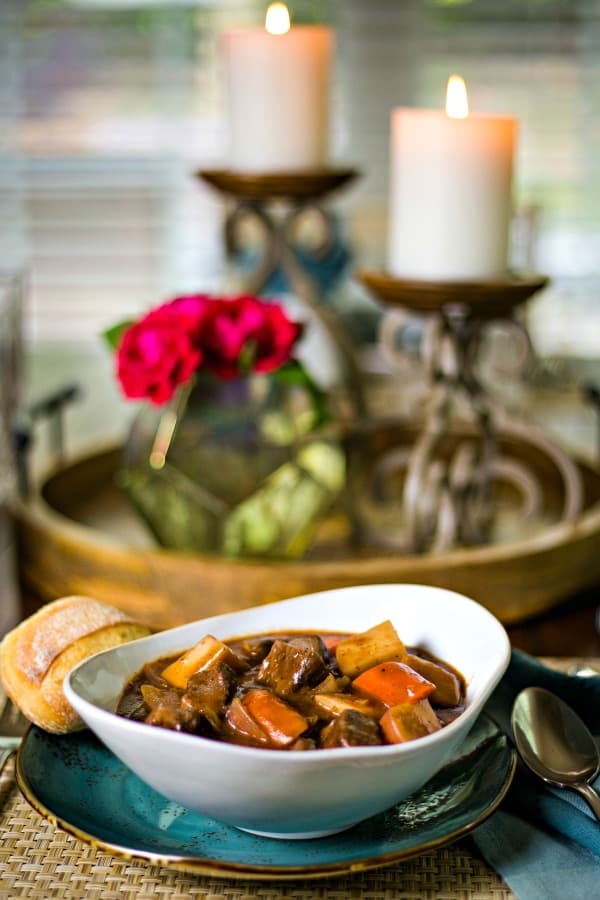 a bowl of beef stew at the dinner table with candles and roses