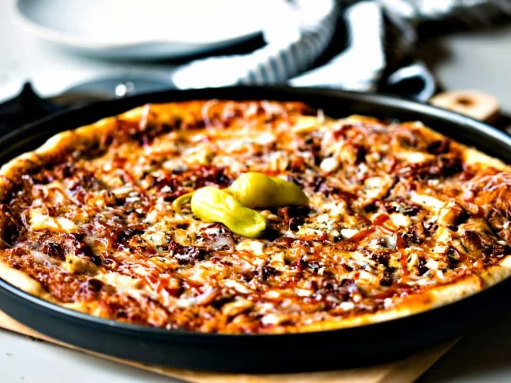 Barbecue Chicken Pizza in a black pizza pan garnished with pepperoncini